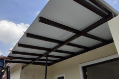 A man is installing an awning roof on a house, working with ACP sheets and panels for a durable finish