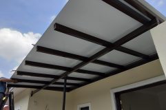A man is installing an awning roof on a house, working with ACP sheets and panels for a durable finish
